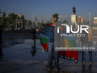 A person holds a Mapuche flag, after being wet by the cart throws water from the riot police of carabineros de Chile (COP) on October 30, 20...