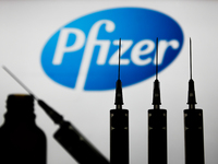 Medical syringes are seen with Pfizer company logo displayed on a screen in the background in this illustration photo taken in Poland on Nov...