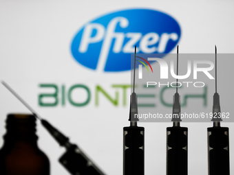 Medical syringes are seen with Pfizer and BioNTech companies logos displayed on a screen in the background in this illustration photo taken...