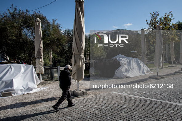 A man with protected mask seen passing by a closed cafe with the Acropolis from behind him in Athens, Greece on November 23, 2020 during the...