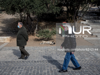 Two men with protected mask seen passing by a sleeping dog at the Acropolis heel in Athens, Greece on November 23, 2020 during the second CO...