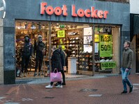 Foot Locker Store with people passing in front of it and a Black Friday sign with sale 50% as seen in the front display window of a shop in...