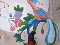 An Iranian woman wearing a protective face mask walks past a mural on a street-side in northern Tehran on day-3 of two-week total lockdown o...