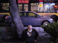 An Iranian man wearing a protective face mask smiles as he sits on a street-side in northern Tehran on day-3 of two-week total lockdown on N...