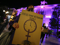 A woman with a sign in front of The City Hall of Granada illuminated in purple during the feminist protest against sexist violence on Novemb...