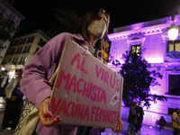 A woman with a sign protests in front of The City Hall of Granada illuminated in purple during the feminist protest against sexist violence...