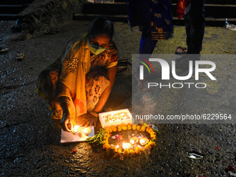A lady wearing mask decorates a river bank with earthen lamps on the eve of Dev Deepawali . Dev Deepawali is a festival of Kartik purnima an...