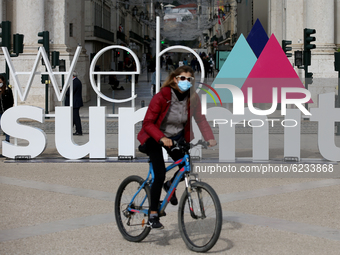A woman wearing a face mask rides a bike past a 3D logo of Web Summit in downtown Lisbon, Portugal on November 30, 2020. Web Summit, Europes...