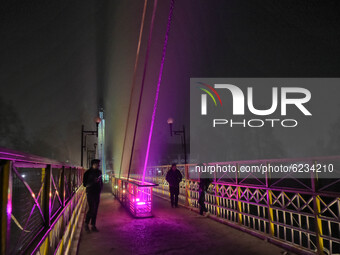 People walk on a illuminated bridge during cold winter evening in Srinagar, Indian Administered Kashmir on 30 November 2020. (