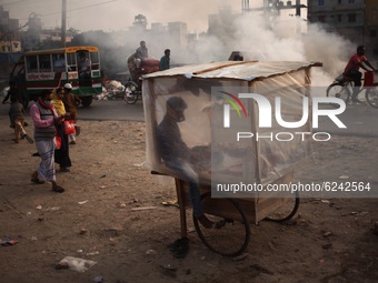 A cake vendor waits for customer inside his polythene wrapped shop as passerby make their move beside a garbage fire  at Keraniganj area in...