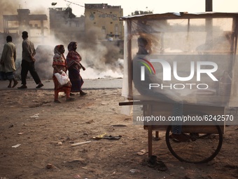 A cake vendor waits for customer inside his polythene wrapped shop as passerby make their move beside a garbage fire  at Keraniganj area in...
