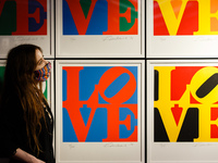 A member of staff wearing a face mask poses with 'The Book of Love', a set of 12 screenprints by American artist Robert Indiana, estimated a...