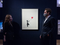 (EDITORIAL USE ONLY) Staff members pose with Banksy's (born 1975) Girl with Balloon, 2004 (est. £120,000 - 180,000) during a photo call for...