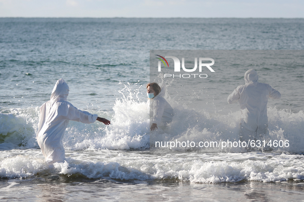 People wearing face masks and protective suits take part in a traditional sea bath to welcome the new year at Carcavelos beach on the outski...