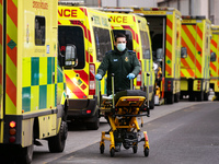A paramedic wearing a face mask pushes a stretcher past ambulances parked outside the emergency department of the Royal London Hospital in L...