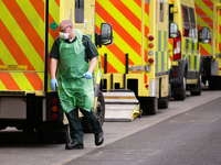 A paramedic wearing PPE walks beside ambulances parked outside the emergency department of the Royal London Hospital in London, England, on...