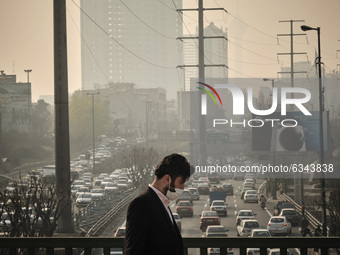 An Iranian man wearing a protective face mask walks along a street-side in northern Tehran during a polluted air, following the COVID-19 out...