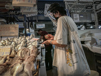 A woman wearing a face shield is selecting and paying for her sea food. Daily life scene in the Varvakios central fish market in downtown At...