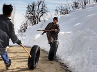 Kashmiri Kids playing with used vehicle Tyres in snow covered People walk in snow covered area of Hajibal on the outskirts of District Baram...