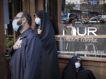 An Iranian man and two veiled women wearing protective face masks beat themselves while attend a religious ceremony to commemorate the death...