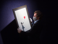A gallery staff member poses with 'Girl with Balloon', 2004, by Banksy (est. £100,000-150,000) during a photo call for Bonhams' British. Coo...