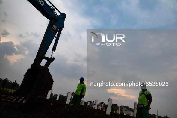 Excavacator help grave digger to close the grave with dirt. Burrial process of a victim of Covid19 at Srengsawah, South Jakarta, Indonesia o...