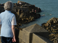 A woman watches swimmers jumping into the water at Forty Foot in Sandycove, Dublin, in fine sunny weather during level 5 COVID-19 lockdown....