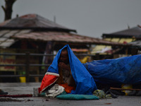 An indian begger uses a plastic sheet shelter from rain,in Allahabad on June 29,2015. (