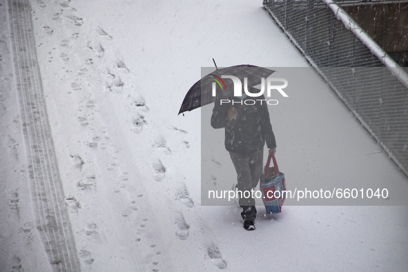 A man is walking on the snow holding an umbrella and wearing a facemask as a Covid-19 coronavirus pandemic measure. The third day of the unu...