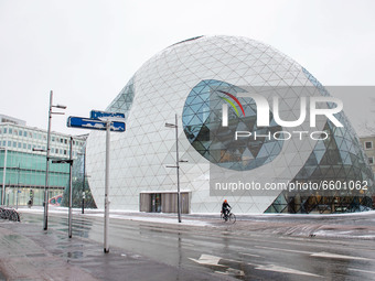 People walking and cycling their bikes in front of De Blob, a modern architecture building, during the snowfall. The third day of the unusua...