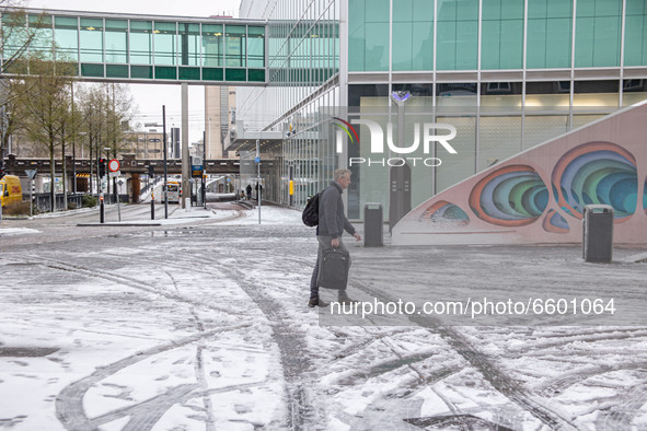 A man holding baggage as seen walking on the melting snow in Einhdoven city center square. The third day of the unusual April snowfall in Th...