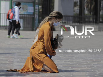 A woman kneels in prayer while carrying her dog in the courtyard of the Basilica of Guadalupe in Mexico City, Mexico, on April 11, 2021, dur...