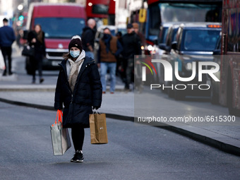 A woman wearing a face mask carries bags of shopping across Oxford Street in London, England, on April 12, 2021. Coronavirus lockdown measur...