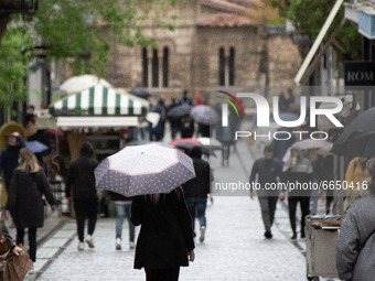 People are walking during a rainy day, wearing protected mask and holding umbrellas at Ermou street in the center of Athens, Greece on April...
