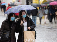 People are walking during a rainy day, wearing protected mask and holding umbrellas at Ermou street in the center of Athens, Greece on April...