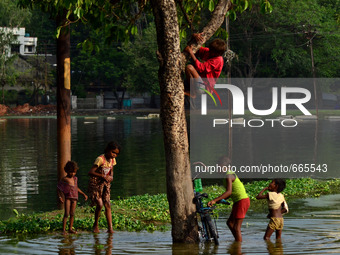 Indian children play in blocked  rain water in a flooded pathway following heavy rain in Allahabad on July 1,2015. (