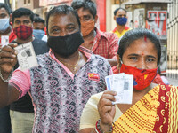People wearing mask shows their voter id card as they queued in front  of a polling station , during 7th phase of West Bengal assembly elect...