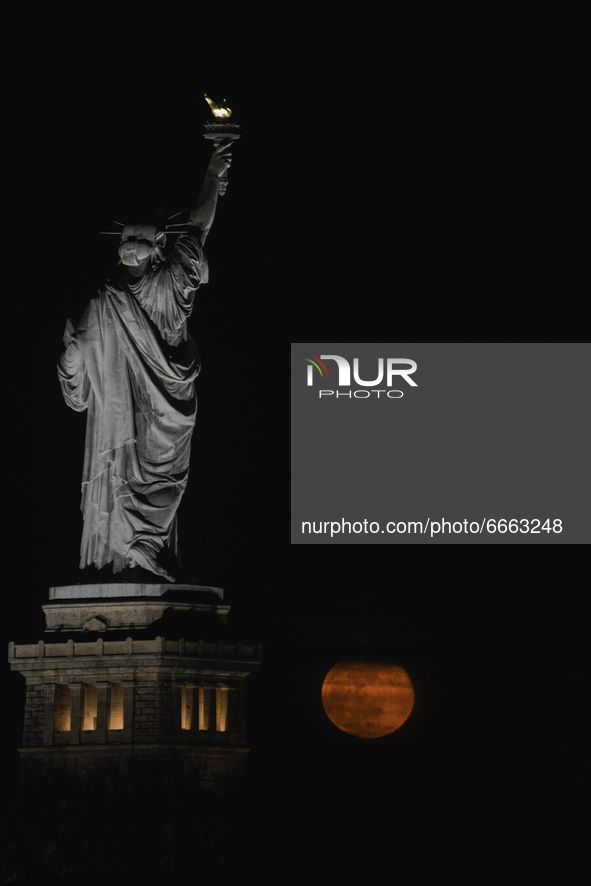 The Super Flower Moon rises behind the Statue of Liberty in New York City, US on April 27, 2021 as seen from Jersey City, New Jersey. 