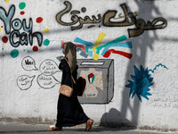 Two Palestinian women walk past a mural painting calling on people to vote during the upcoming elections (legislative in May and presidentia...