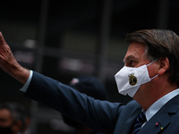Brazil's President Jair Bolsonaro gestures to supporters wearing a protective face mask before a press conference amidst the Coronavirus (CO...