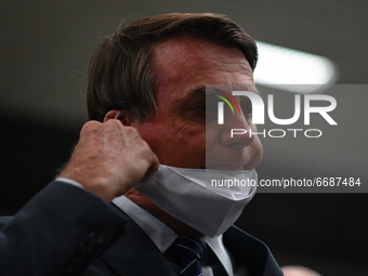 Brazil's President Jair Bolsonaro removes his protective face mask to speak to journalists during a press conference amidst the Coronavirus...