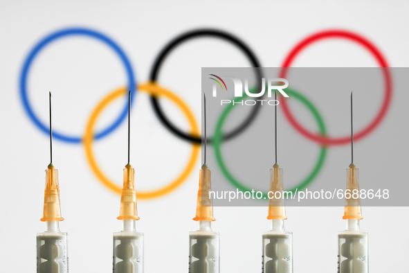 Medical syringes are seen with the Olympic rings displayed on a screen in the background in this illustration photo taken in Krakow, Poland...