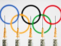 Medical syringes are seen with the Olympic rings displayed on a screen in the background in this illustration photo taken in Krakow, Poland...