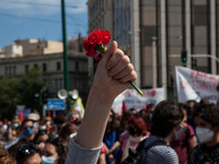 Members of the communist party - affiliated PAME wearing protective face masks hold flags and red carnations, as they protest during a rally...