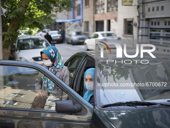 An Iranian elderly woman wearing a protective face mask sits in a vehicle out of a health center while waiting to receive a dose of China's...