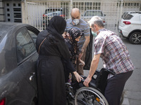 Relatives of an Iranian elderly woman (C) help her for sitting on a wheelchair out of a health center as she arrives tp receive a dose of Ch...