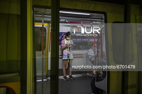 A Women wearing a face mask looks at her phone while riding in the MTR in Hong Kong, Monday, May 10, 2021. 