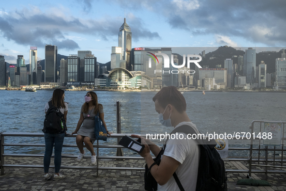 Two Women Chat and a man looks at his phone in front of the Hong Kong City Skyline in Hong Kong, Monday, May 10, 2021. 