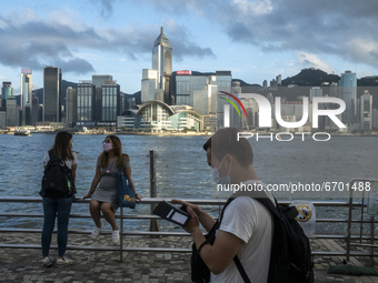 Two Women Chat and a man looks at his phone in front of the Hong Kong City Skyline in Hong Kong, Monday, May 10, 2021. (