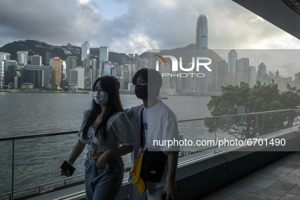 A Couple wearing face masks walks pass the Hong Kong City Skyline in Hong Kong, Monday, May 10, 2021. 